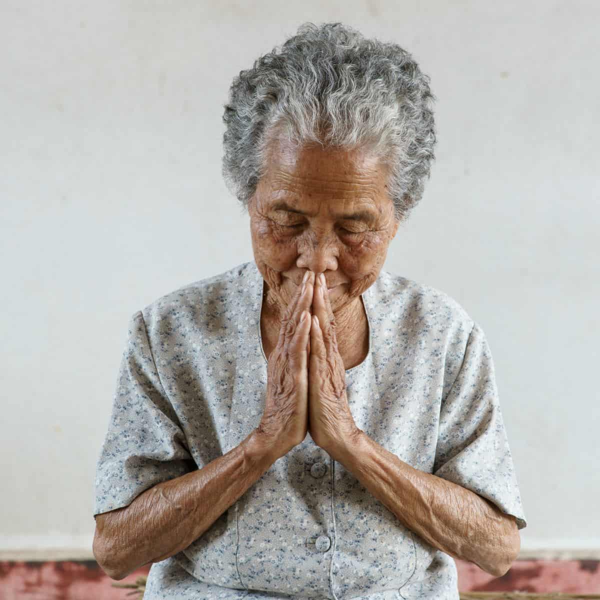Older woman with dark skin praying with hands folded